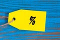 Percent symbol of cloth on yellow tag at blue wooden background. Design for sale, discount, advertising, marketing price