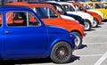 A row of colorful Fiat 500s in a roadside parking lot, waiting to participate in an auto gathering later.