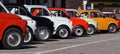 A row of colorful Fiat 500s in a roadside parking lot, waiting to participate in an auto gathering later