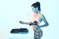 Percussion handheld massager, athletic young girl choose attachments in suitcase for massaging gun in neon studio light