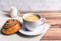 Perfect breakfast of a homemade cinnamon bun, coffee and glass milk jug on wooden table. Rustic style. Royalty Free Stock Photo