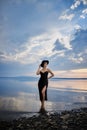 Perfect brunette beauty woman in a black hat and a black dress poses near a lake against a blue sky. Long hair woman and beautiful Royalty Free Stock Photo