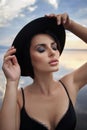 Perfect brunette beauty woman in a black hat and a black dress poses near a lake against a blue sky. Long hair woman and beautiful Royalty Free Stock Photo