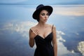 Perfect brunette beauty woman in a black hat and a black dress poses near a lake against a blue sky. Long hair woman and beautiful Royalty Free Stock Photo