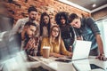 Group of six cheerful young people looking at laptop with smile while leaning to the table in office Royalty Free Stock Photo
