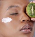 Perfect day for a pamper session. Studio shot of an attractive young woman holding kiwi fruit to her face.