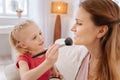 Positive skillful girl putting powder on her mothers face