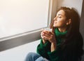 Perfect morning A young brunette woman sits on a windowsill and holds a cup of tea or coffee in her hands. Female model Royalty Free Stock Photo