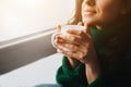 Perfect morning A young brunette woman sits on a windowsill and holds a cup of tea or coffee in her hands. Female model Royalty Free Stock Photo