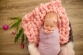 Perfect newborn baby girl in pink blanket in a wicker basket decorated with beautiful pink tulips