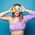 Perfect pretty happy woman looking through bright colorful donuts against blue studio wall background Royalty Free Stock Photo