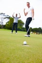 The perfect putt. Low angle shot of a golf ball approaching the hole while two golfers look on. Royalty Free Stock Photo