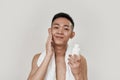 Perfect skin. Portrait of shirtless young asian man with towel around his neck looking at camera, applying lotion after Royalty Free Stock Photo