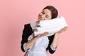 Portrait of young Caucasian chambermaid with clean towels isolated over pink background