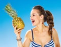 Cheerful young woman on seashore wanting to bite pineapple