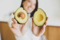 Perfectly ripe avocado halves in hands of happy woman in modern kitchen, close up. Healthy eating Royalty Free Stock Photo