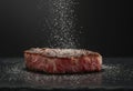 Perfectly seared medium-rare steak on black slate plate with sea salt crystals, set against a dark blurred background