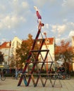 A performance artist balances on top of a house of cards