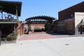 A performance stage made of red brick with a brown wooden pergola on top with tall black curved light posts i