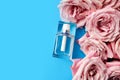 Perfume glass bottle and pink roses on blue background