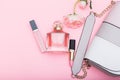 Perfume, lip gloss, lipstick and bag on a pink background