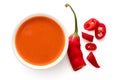 Peri peri chilli sauce in a white ceramic bowl next to a cut up chilli pepper isolated on white from above