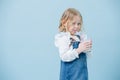 Perky little girl in jeans overalls sipping milkshake through a straw over blue