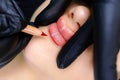 Permanent makeup master in black gloves holds the lips of the model and paints the lips with a red pencil Royalty Free Stock Photo