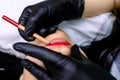 Permanent makeup master in black gloves holds lips and paints over with a red pencil to perform a tattoo Royalty Free Stock Photo