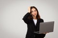 Perplexed young professional woman holding a laptop, scratching her head with a puzzled expression Royalty Free Stock Photo