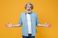 Perplexed worried elderly gray-haired mustache bearded man in casual blue shirt posing isolated on yellow background