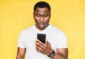Perplexed and worried handsome African American man holds smartphone, stares with surprised expression.