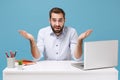 Perplexed young bearded man in light shirt sit and work at desk with pc laptop isolated on pastel blue background Royalty Free Stock Photo