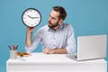 Perplexed young bearded man in light shirt sit and work at white desk with pc laptop isolated on pastel blue background Royalty Free Stock Photo