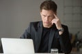 Perplexed young businessman looking at laptop screen at workplac