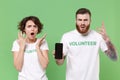 Perplexed young friends couple in white volunteer t-shirt isolated on green background. Voluntary free work assistance Royalty Free Stock Photo