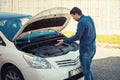 Perplexed young male driver looking confused under the popped hood of his car. Broken transportation, vehicles problems and