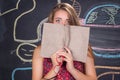 Perplexed young student girl hides behind a book