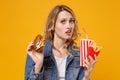 Perplexed young woman in denim clothes isolated on orange background. Proper nutrition or American classic fast food Royalty Free Stock Photo