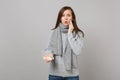 Perplexed young woman in gray sweater, scarf put hand on cheek, holding daily pill box isolated on grey wall background