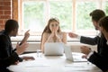 Perplexed young woman looking at coworkers pointing fingers at h