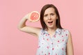 Perplexed young woman in summer clothes hold in hand half of fresh ripe grapefruit isolated on pink pastel wall Royalty Free Stock Photo