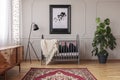 Persian carpet on the floor of mid century baby room interior with grey wooden crib, industrial black lamp and monster plant in