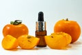 Persimmon fruit oil on a white background. Ripe persimmon fruits and extract in a cosmetic bottle with a dropper. Essential