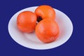 Persimmon fruit on white plate on blue background Royalty Free Stock Photo