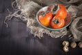 The persimmon in a plate on a napkin made of canvas on a dark wooden table