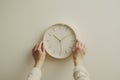 person adjusting a plain analog wall clock, minimal decor