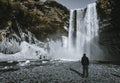 A person admirnig the beauty of Skogafoss waterfall with rainbow located in Iceland.