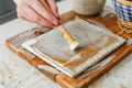 person applying mod podge to a ceramic tile with a brush, decoupage crafting