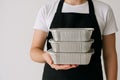 Person holding a stack of three foil food containers with a black apron on a white background Royalty Free Stock Photo
